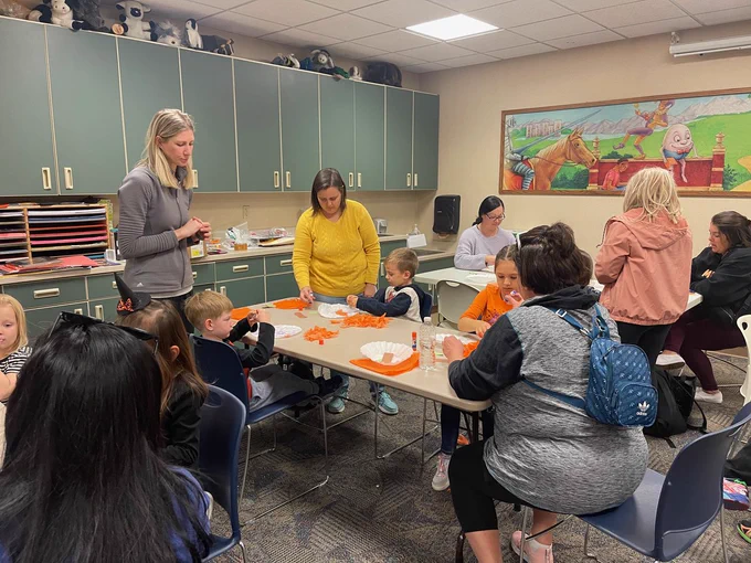 Room full of adults and kids working at tables covered in bright orange tissue paper pieces