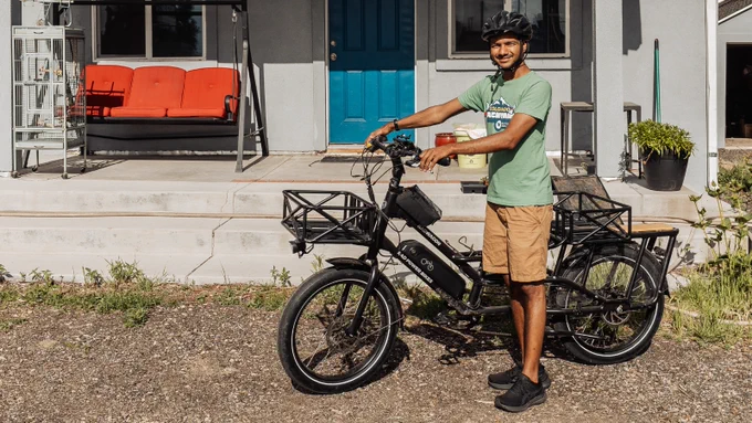 E-bike rebate recipient standing next to an electric cargo bike in front of a modern house with a porch.