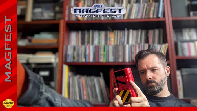 Bit Shifter sits stretched across the bottom of the image, looking very focused on the red original Gameboy they are holding. They sit in front of a blurred bookcase full of items.
