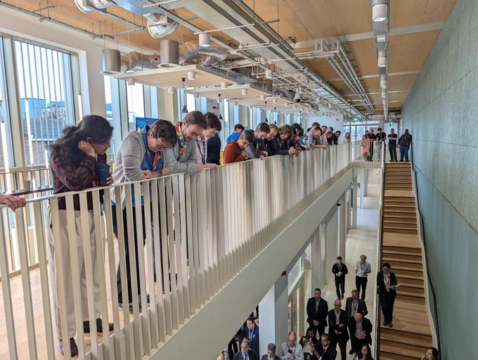 Members of NQCC staff leaning over a balcony and standing on stairs looking down to watch Minister Vallance's speech.