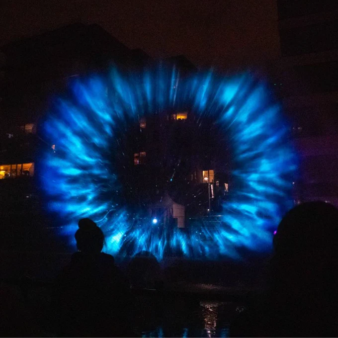 Monad at Leeds Dock. A large blue circle illuminates water spraying up.