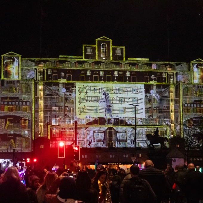 The BookBinder at City Square. The Queens Hotel is projected with illustrations of buildings and a musical note sheet.