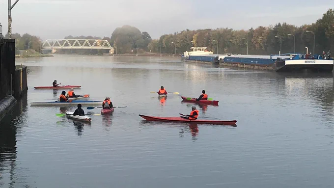 Acht Kayaks in der Zufahrt der Schleuse Flaesheim, im Hintergrund ein Fluss-Schiff.