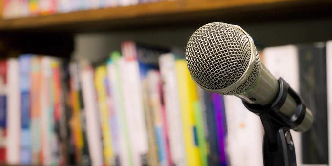 A photo of a microphone on a stand sitting in front of a shelf full of books.