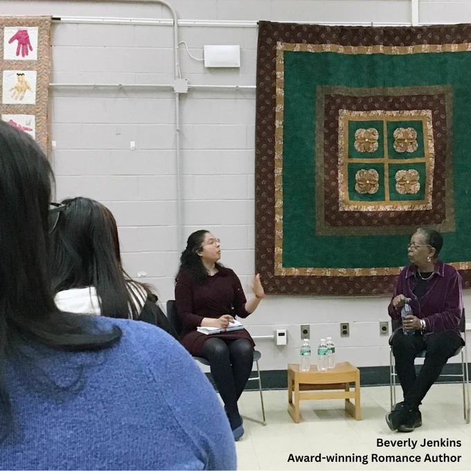 Woman interviews author Beverly Jenkins at the Codman Square branch of the Boston Public Library, in a room filled with fans