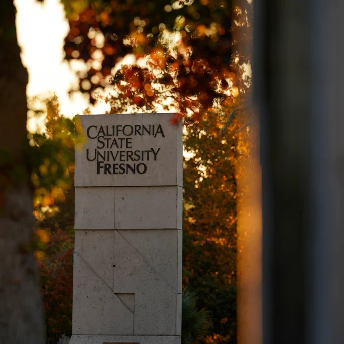 Fresno State Veterans Monument framed by blurred foliage and warm sunset light.