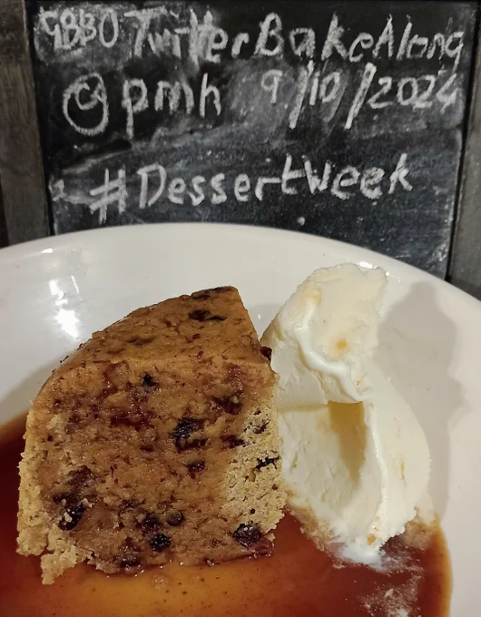A slice of spotted dick in a large bowl with dark thin syrup drizzled over it and a scoop of ice cream