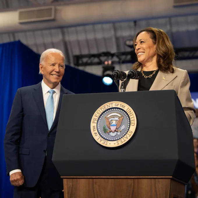 President Joe Biden and Vice President Kamala Harris stand smiling behind a podium at an event.