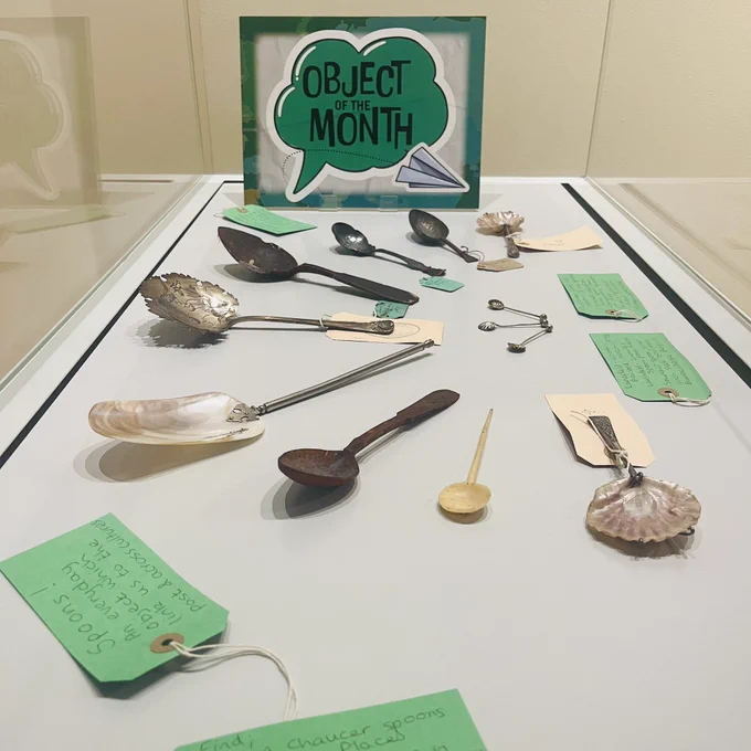 a museum display of spoons made of various materials, some very small and some much larger. A green panel in the case reads ‘Object of the month’ inside a green speech bubble.