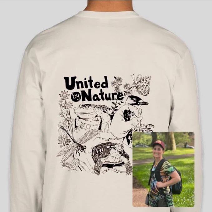 A crème colored tshirt depicting hands holding fabulous critters (bullfrog, box turtle, and red-cockaded woodpecker), a dragonfly and butterfly along with plants and flowers, and sports our 2025 theme “United by Nature.” A profile picture of our tshirt designer Casey is in the bottom right corner.