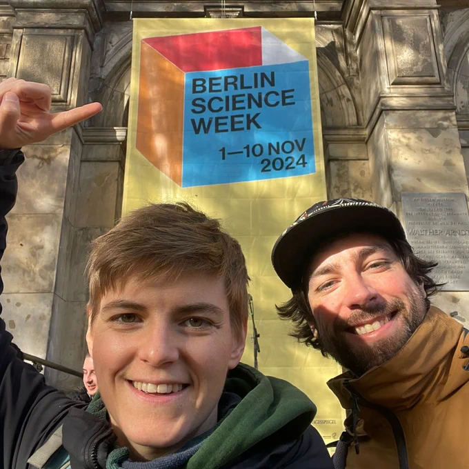 Dr. Annika Kreikenbohm und Chris Spatschek vor dem Museum für Naturkunde Berlin, auf einem Baner ist das Logo der Berlin Science Week abgebildet. 