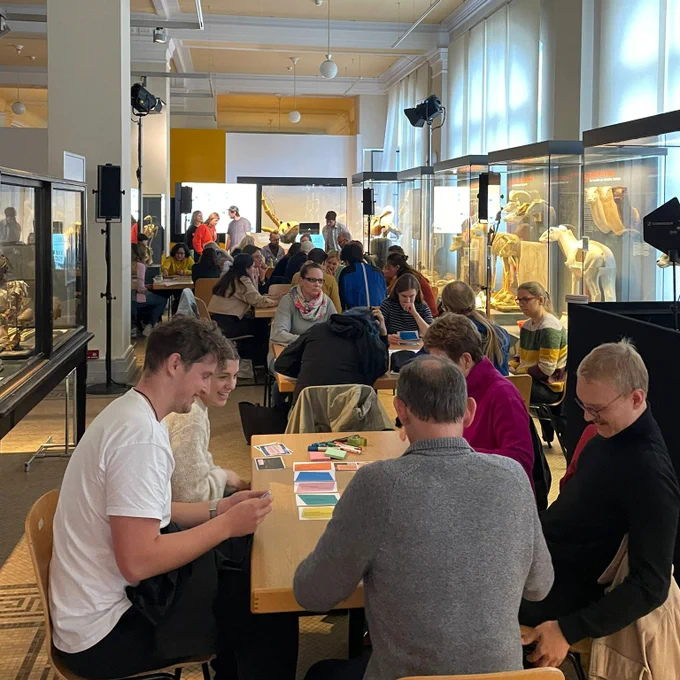 Eine Gruppe von Teilnehmenden während der Berlin Science Week, die im Museum für Naturkunde Berlin an Tischen in einem Raum mit Glasvitrinen sitzt und konzentriert arbeitet. 