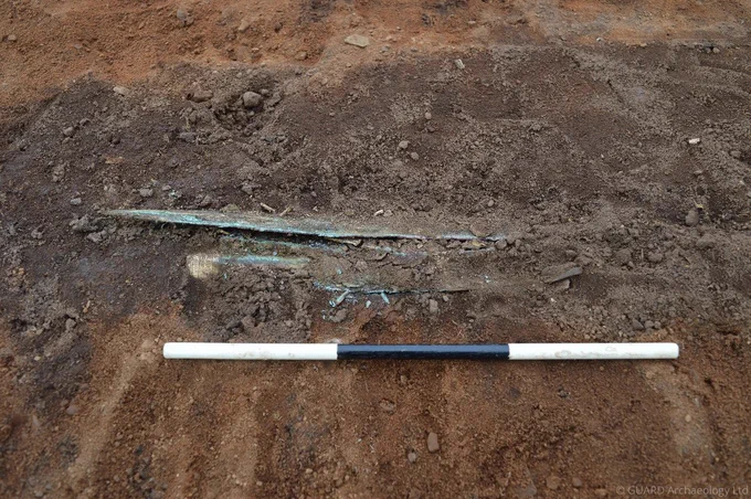 Bronze (now green) sword with gold ornamentation being unearthed from the ground
