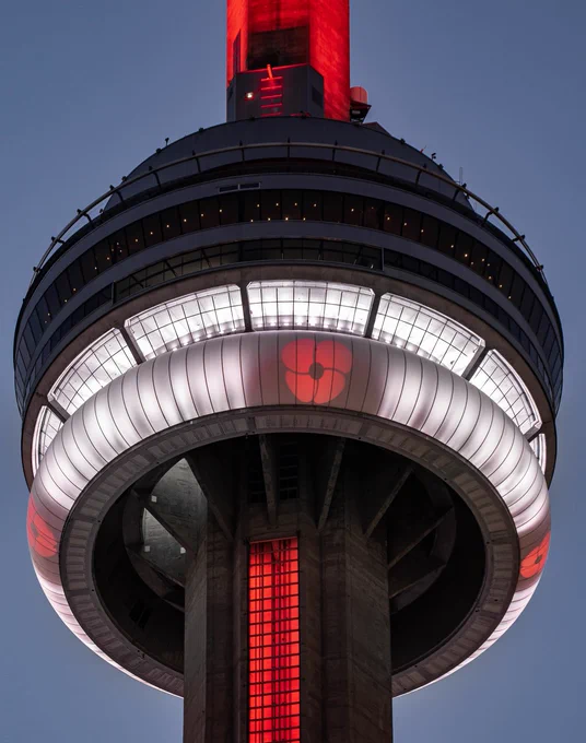 Closeup of the CN Tower at night lit in red and white with projections of red poppies / Gros plan de la Tour CN de nuit, illuminée en rouge et blanc avec des projections de coquelicots rougesv