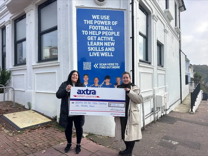 Two women holding up a large cheque from Axtra outside the BHAFC Foundation Community Hub