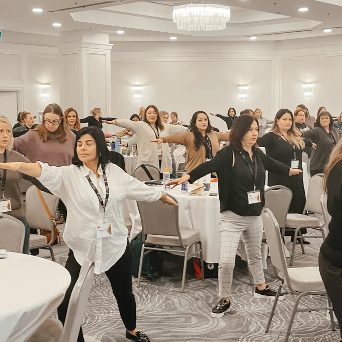 Attendees perform a mindful exercise, holding a yoga pose in a conference room.

