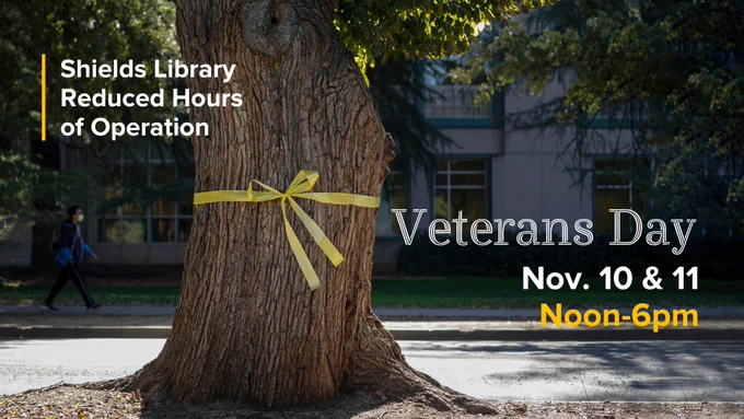 A tree trunk with a yellow ribbon tied around the trunk. Text on top reads “Shields Library Reduced Hours of Operation”.  The text below reads “Veteran’s Day, Nov. 10 & 11, Noon-6pm”.
