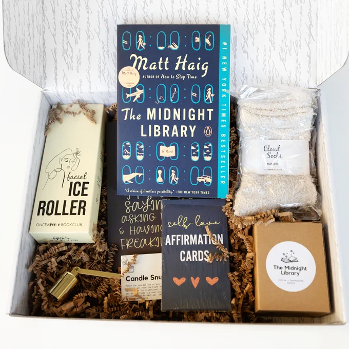 The Midnight Library book with socks, facial ice roller, cards, candle box, candle snuffer in an open box
