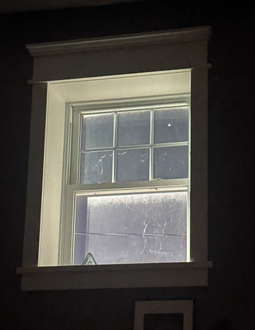Window in the darkness with a small dot of light (Jupiter) visible in the top right corner. Spider webs are also visible on the outside of the window.