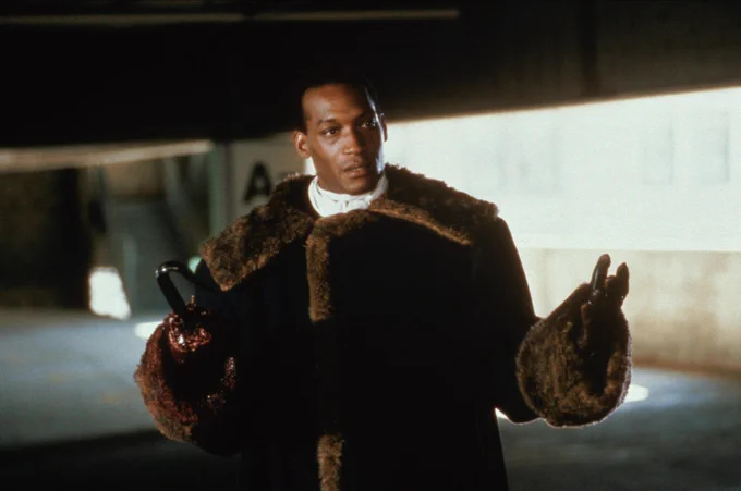 Tony Todd wearing a lavish fur coat with a hook for his right hand, stands in a parking garage in a scene from Candyman