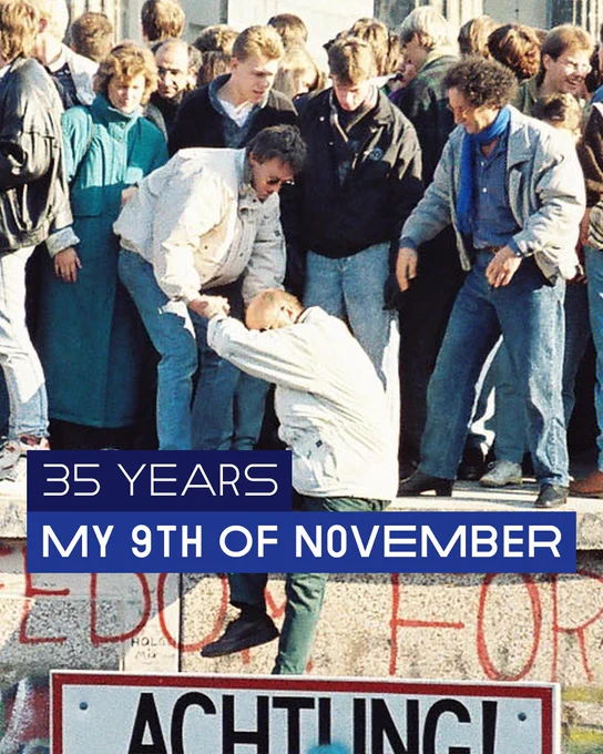 Image of people standing on top of the Berlin Wall on or around November 9, 1989, with one person pulling up another one onto the wall. © Sue Ream / CC by 3.0 DE