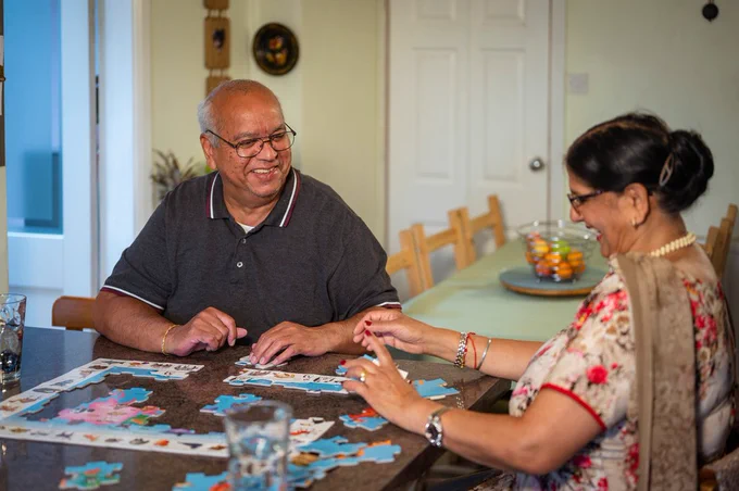 Photo of two older people sat at a table doing a puzzle. They are laughing and smiling. Credit by Peter Kindersley via Centre for Ageing Better_couple with jigsaw