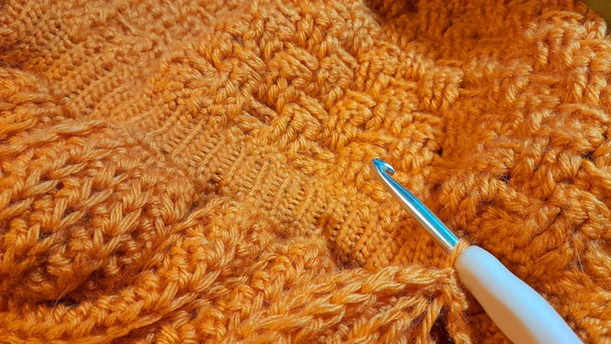 A close up of a crochet project fills the entire photo. There are three different stitches from top to bottom, and a pink crochet hook sits on the bottom right of the photo.