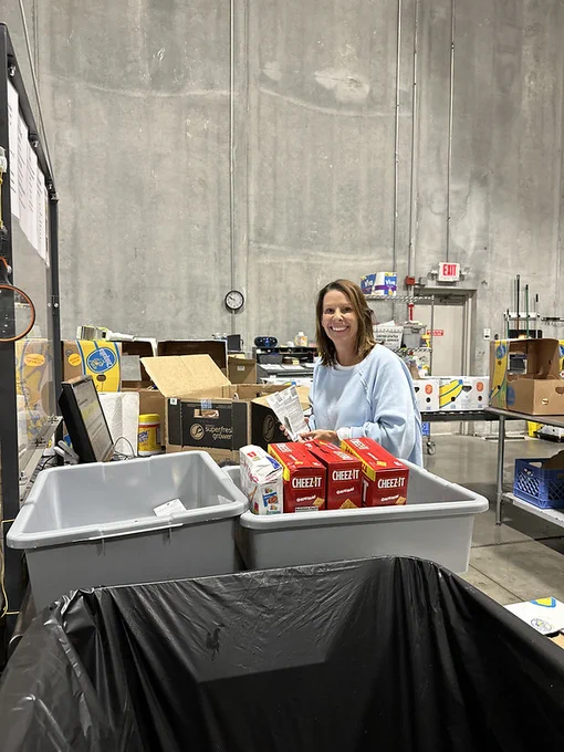 Person smiling next to a bin of Cheez-It crackers in a warehouse setting with various boxes and containers around.