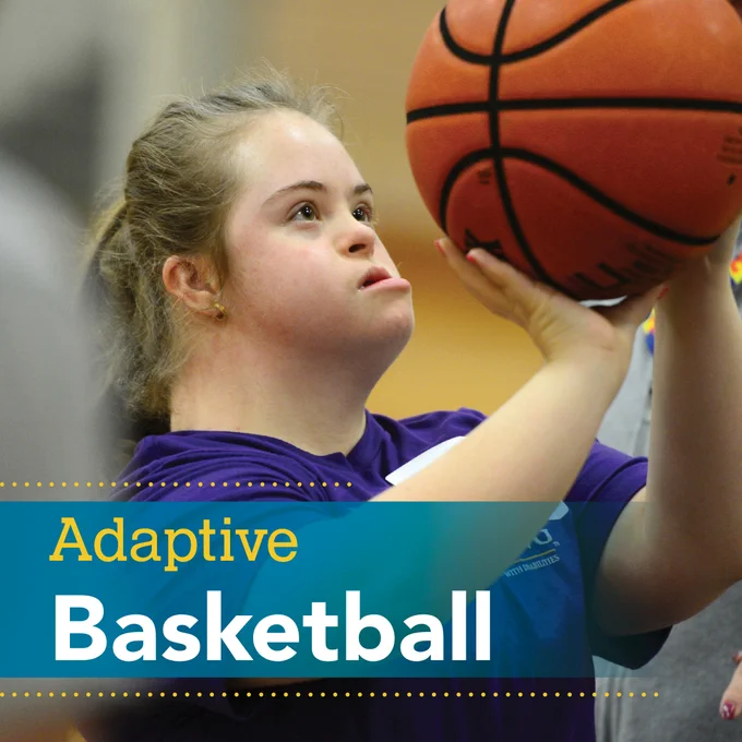 A young girl with down syndrome holding a basketball at face-level getting ready to shoot into the basket. Adaptive basketball 
