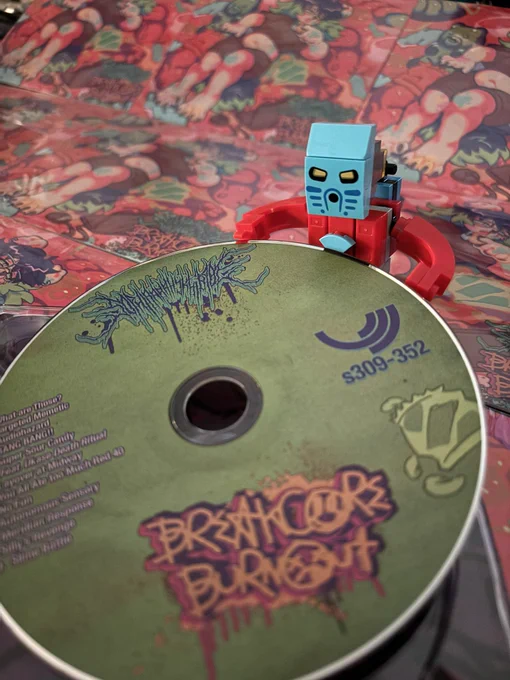 lego bionicle Takua lifts a copy on CD out of its case. there numerous cd cases lined up in the background.