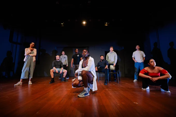 Nine young people pose in a dimly lit space