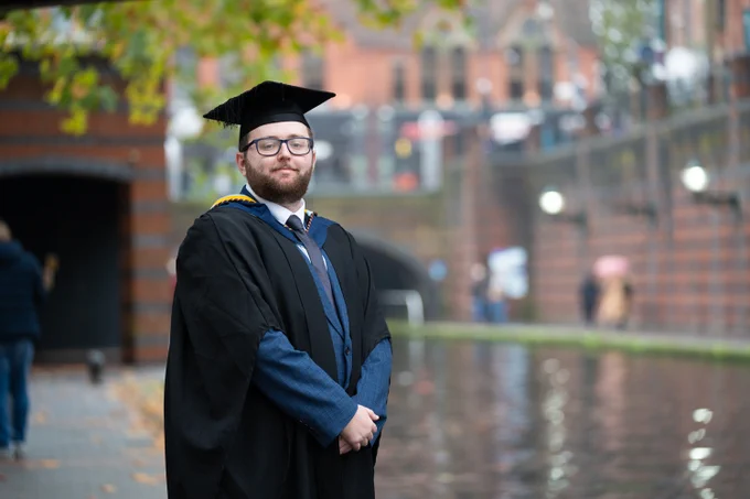 Student dressed in Graduation attire posing by canal