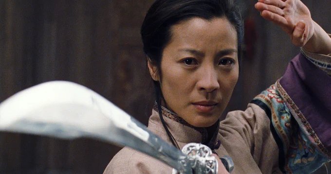 Michelle Yeoh in an intense action scene from the movie Crouching Tiger, Hidden Dragon, holding a sword in a dynamic pose.