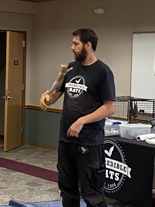 A person in an Incredible Bats t shirt letting a small creature similar to a squirrel climb up his arm
