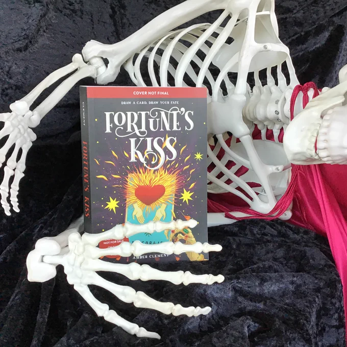 A skeleton lying on its side clutching the book. The book cover shows a loteria card with a heart bursting into flames