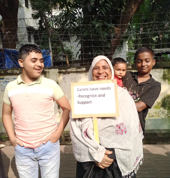 Woman and children standing outside, woman holding placard reading "Carers have needs - Recognise and support"