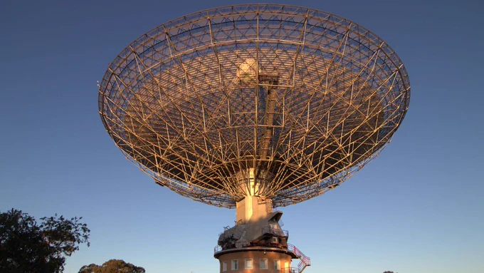 Image shows CSIRO's Murriyang, our Parkes radio telescope, on Wiradjuri Country in NSW. The majestic telescope is glowing in golden hour sunlight.