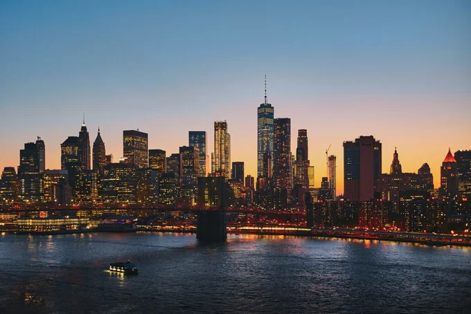 A photo of thr New York City skyline at night. A river is in the foreground.