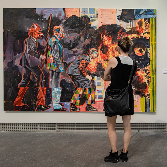 Visitor observing a colorful contemporary painting by Nicky Nodjoumi depicting three figures in an abstract style on view in YBCA's gallery.