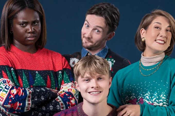 A photo showing four individuals in Christmas jumpers smiling on stage 