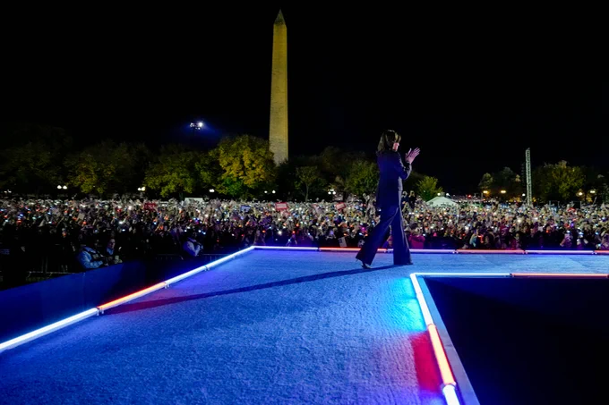 Vice President walking on stage during a campaign event at the Ellipse in Washington D.C. Surrounding her is a crowd of supporters and the Washington Monument in view. 