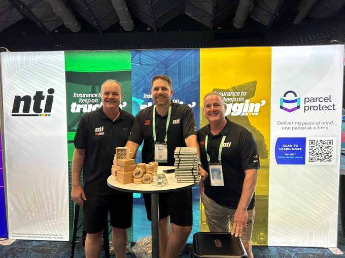 Three people stand behind a promotional booth with branded banners for "NTI" and "Parcel Protect" at an insurance conference. Left to right: Sergio Sartor, Jason Rogerson, Rick Griffin.