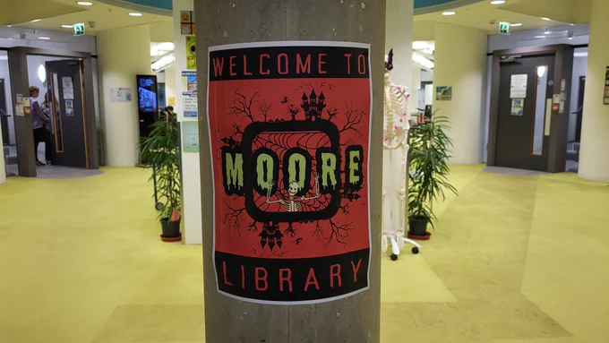 Photo of Moore library entrance with halloween posters "Welcome to Moore Library" with skeletons and halloween themed fonts