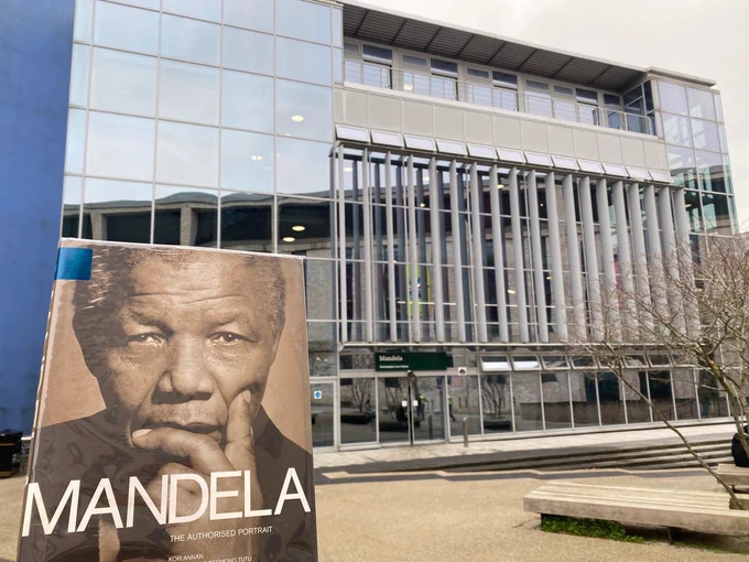 Image shows someone holding a book about Mandela in front of the Mandela Building