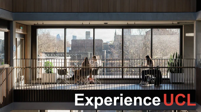 View from inside a UCL building looking out through large windows to a balcony where several individuals are seated at tables, with city buildings visible in the background.