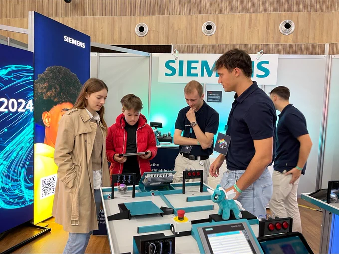 Zwei Siemens-Azubis stehen mit zwei Kindern an einem Experimentiertisch. 