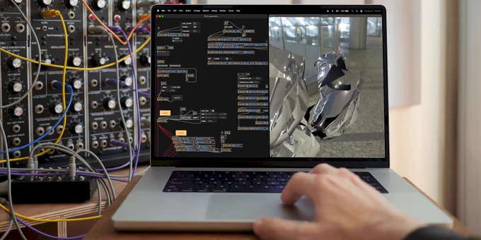 A MacBook Pro running the new 3D geometry tools, a modular in the background, and a hand on the trackpad. Display shows a shiny reflective metal geometry in a scene with a patch interface on the left.