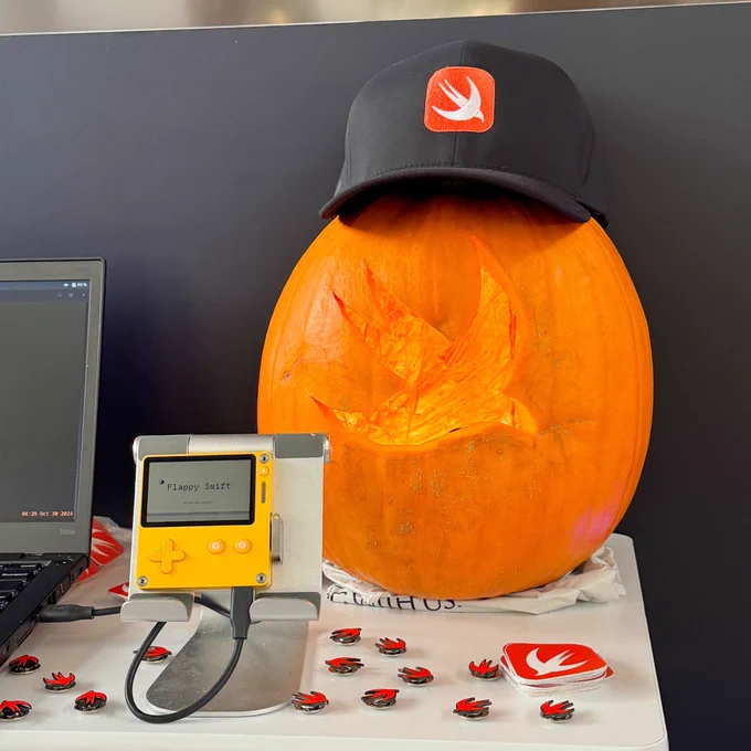 From the booth at GitHub Universe, a Playdate portable game console running a Swift-powered game, a Swift-themed pumpkin and baseball cap, and some other Swift swag.