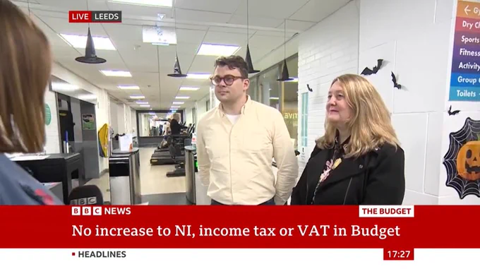 Good Things CEO, Helen Milner smiles during an interview with BBC News. There is a banner displaying headlines about No increase to NI income tax or VAT in Budget. The setting is indoors in a gym in Pudsey, Leeds.