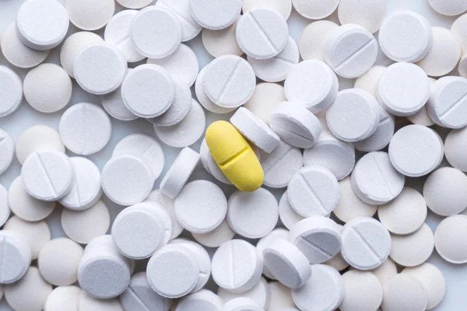 A pile of white round pills. There is a yellow pill in the middle. 
